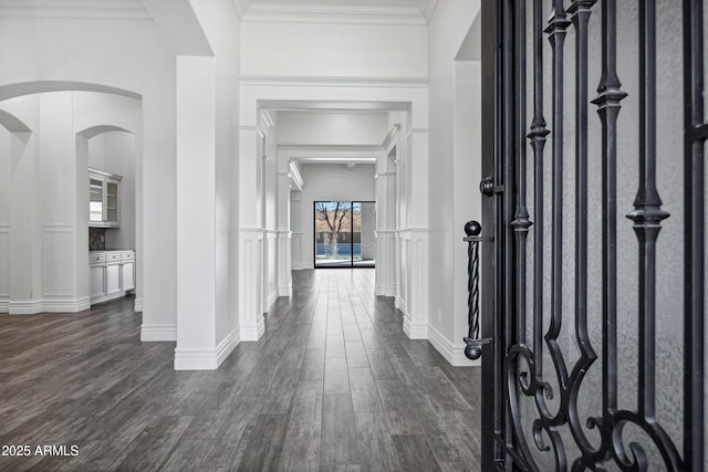 hall with arched walkways, dark wood finished floors, a wainscoted wall, ornamental molding, and a decorative wall