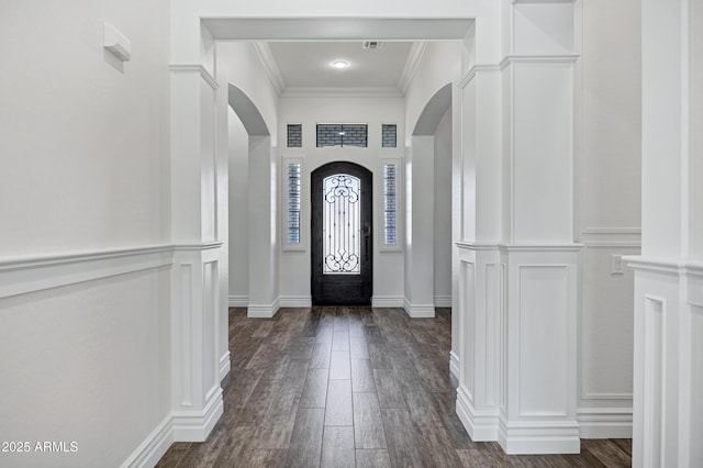 foyer entrance with dark wood-style floors, arched walkways, crown molding, visible vents, and a decorative wall