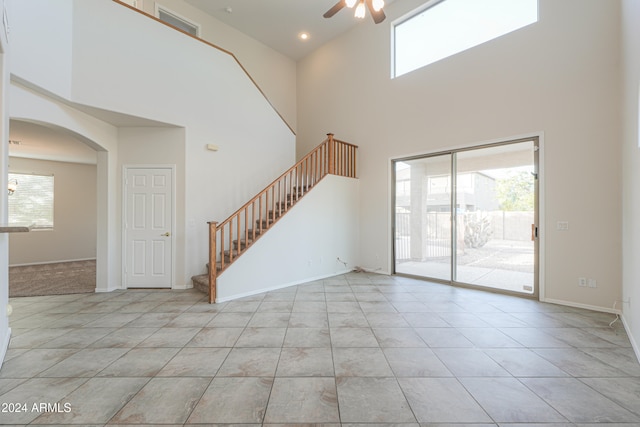 unfurnished living room with a wealth of natural light, ceiling fan, light tile patterned floors, and a high ceiling