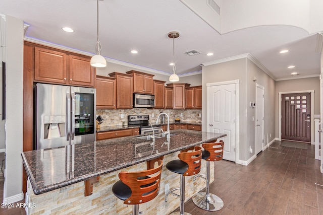 kitchen with a center island with sink, appliances with stainless steel finishes, decorative light fixtures, a kitchen bar, and dark wood-type flooring