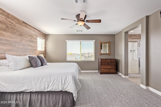 bedroom with ensuite bathroom, ceiling fan, wooden walls, and light carpet