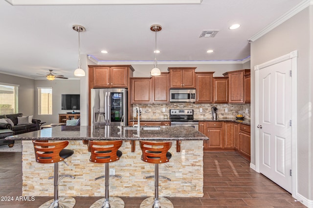 kitchen with sink, an island with sink, a kitchen breakfast bar, pendant lighting, and appliances with stainless steel finishes