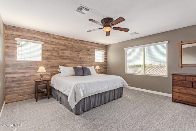 carpeted bedroom featuring ceiling fan, multiple windows, and wooden walls