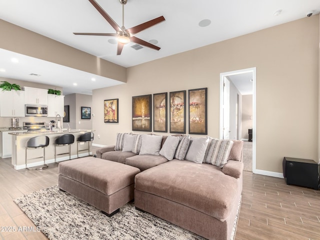 living room with ceiling fan, sink, and light wood-type flooring