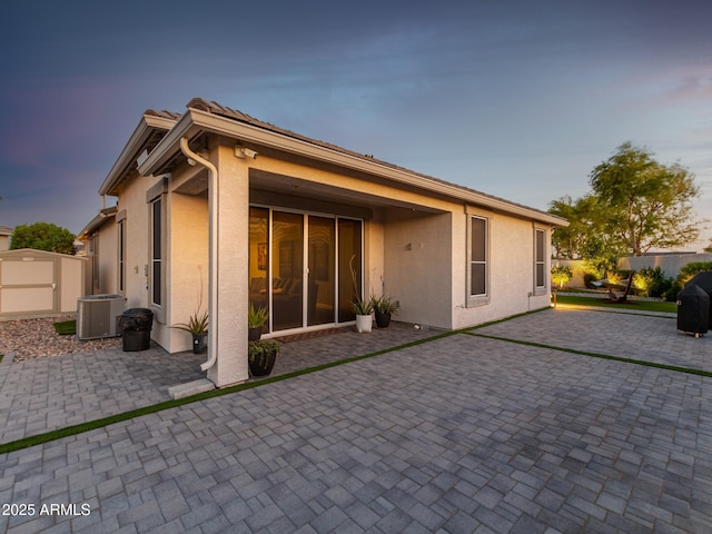 back house at dusk featuring central AC unit and a patio area