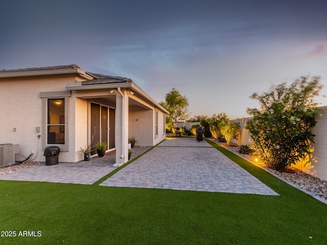 yard at dusk featuring central AC and a patio