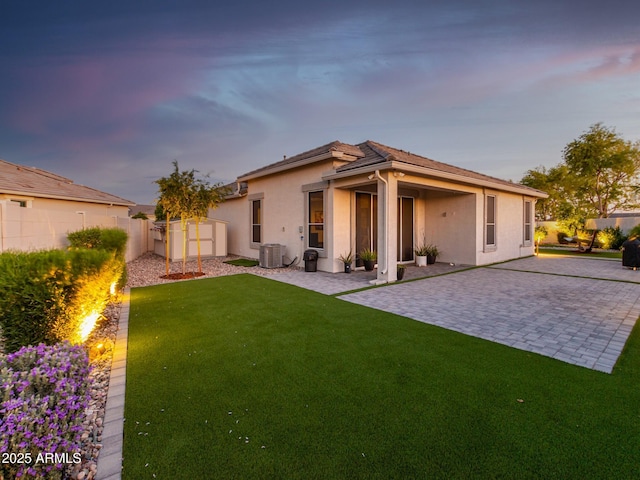 back house at dusk with a patio area, cooling unit, and a yard