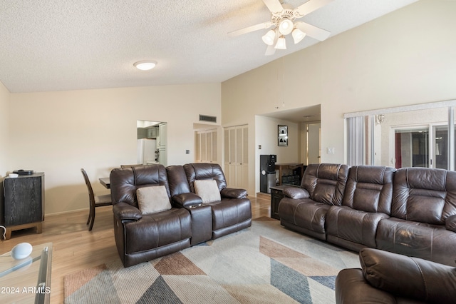 living room with ceiling fan, light hardwood / wood-style flooring, high vaulted ceiling, and a textured ceiling