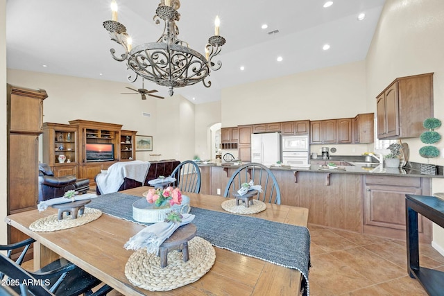 dining area featuring light tile patterned flooring, a high ceiling, ceiling fan with notable chandelier, and sink