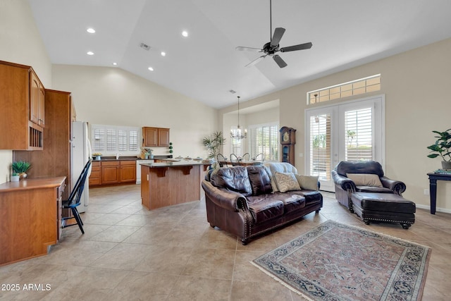 tiled living room with ceiling fan with notable chandelier and high vaulted ceiling