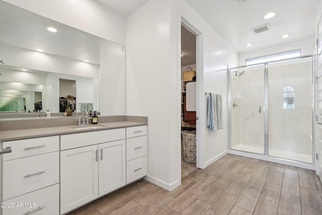 bathroom featuring a stall shower, wood finished floors, a walk in closet, recessed lighting, and vanity
