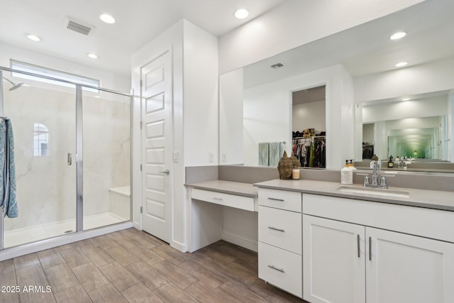 full bathroom featuring a stall shower, vanity, wood finished floors, a walk in closet, and recessed lighting