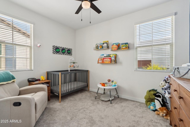 carpeted bedroom featuring a crib, multiple windows, baseboards, and a ceiling fan