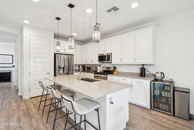 kitchen with appliances with stainless steel finishes, wine cooler, a sink, wood finish floors, and a breakfast bar area