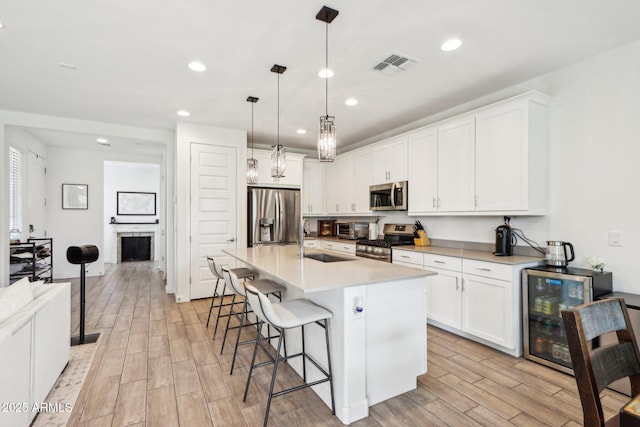 kitchen featuring stainless steel appliances, a sink, wine cooler, light wood-style flooring, and a kitchen bar