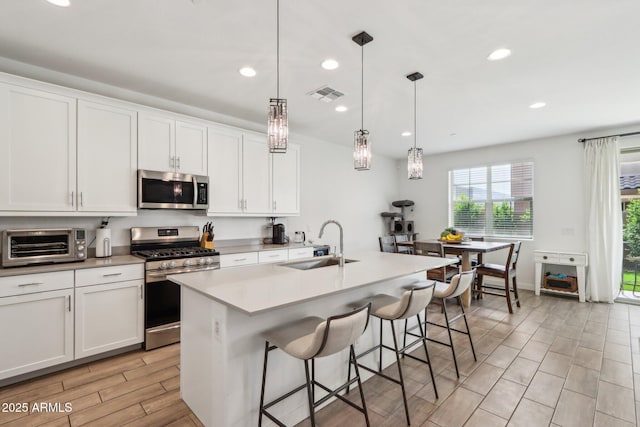 kitchen with stainless steel appliances, a sink, wood tiled floors, recessed lighting, and light countertops