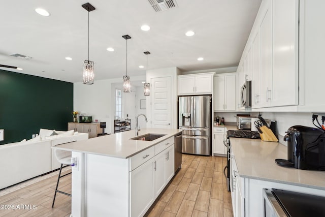 kitchen featuring a sink, appliances with stainless steel finishes, open floor plan, recessed lighting, and light wood-style floors