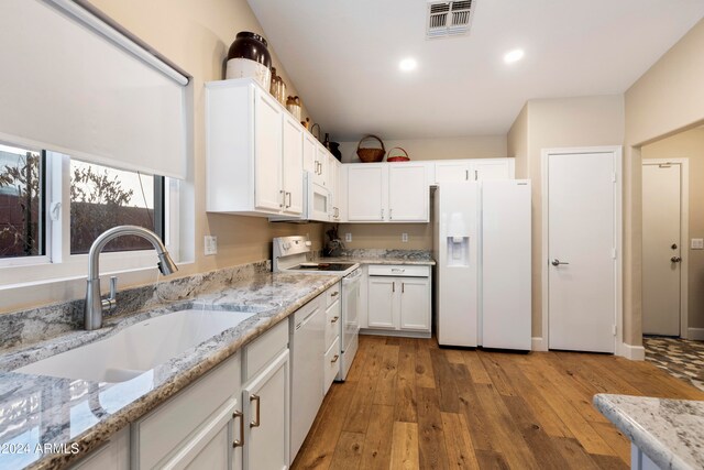 kitchen with light stone counters, white appliances, sink, light hardwood / wood-style floors, and white cabinetry