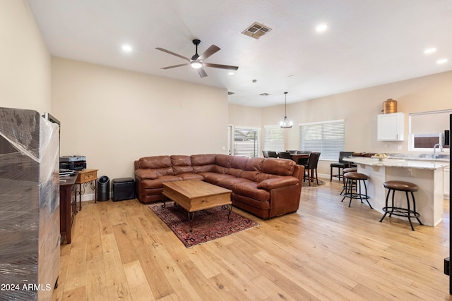 living room with ceiling fan with notable chandelier and light hardwood / wood-style floors