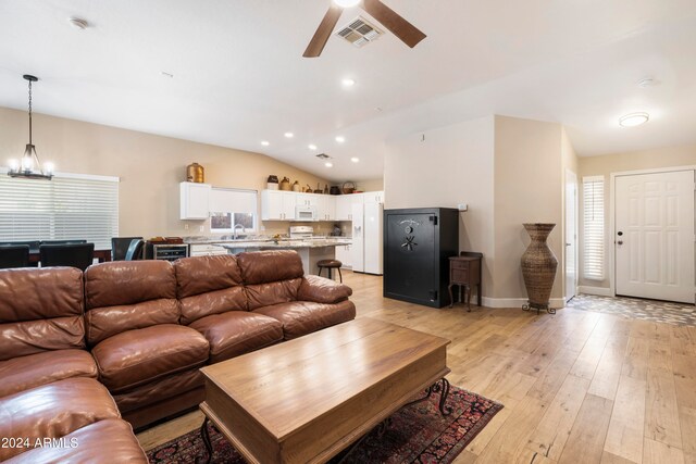 living room featuring plenty of natural light, light hardwood / wood-style floors, ceiling fan with notable chandelier, and vaulted ceiling