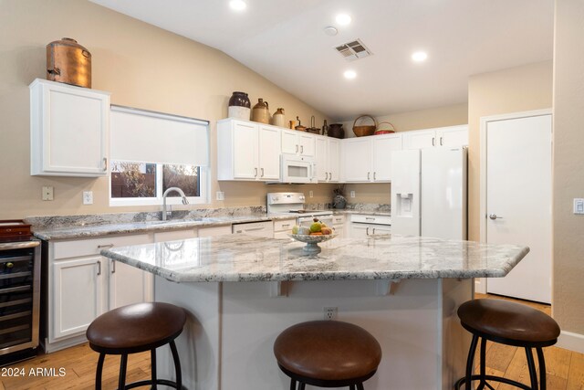 kitchen with a center island, lofted ceiling, white appliances, white cabinets, and a kitchen breakfast bar