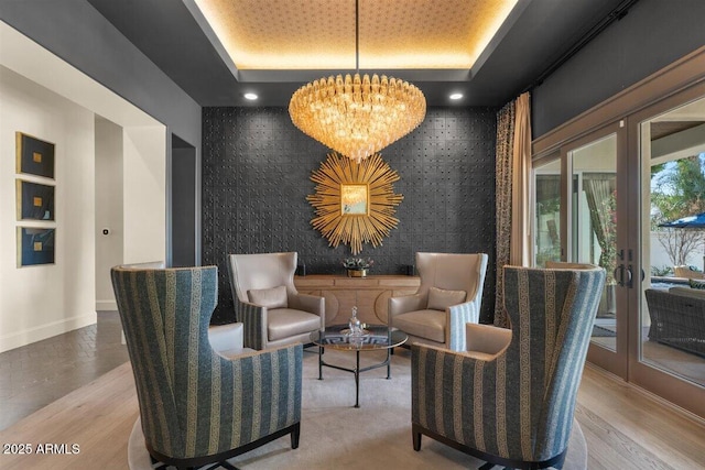 sitting room with a tray ceiling, light hardwood / wood-style flooring, a notable chandelier, and french doors