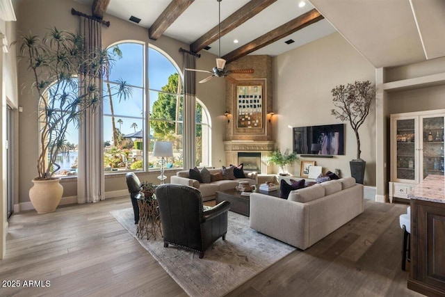 living room featuring beam ceiling, a premium fireplace, ceiling fan, and light wood-type flooring