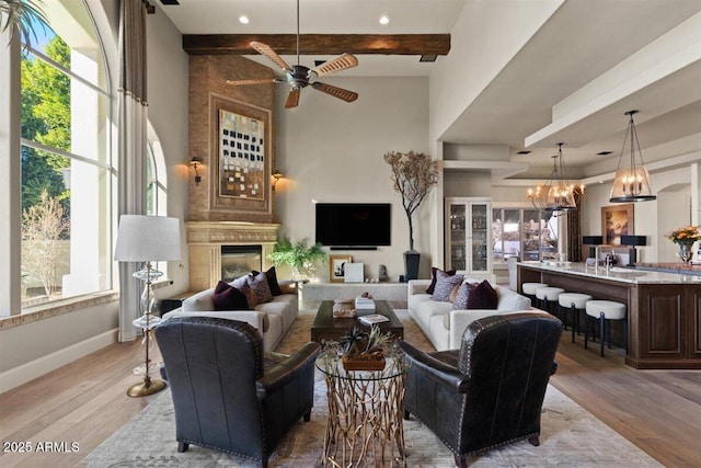 living room featuring a high end fireplace, ceiling fan with notable chandelier, beam ceiling, and light hardwood / wood-style flooring