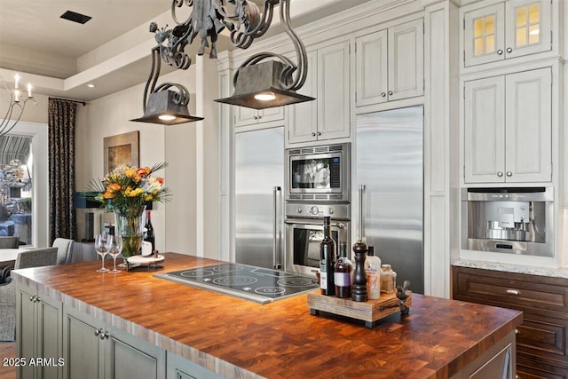 kitchen with white cabinetry, an inviting chandelier, a center island, built in appliances, and wood counters