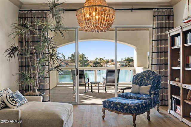 sitting room with a water view, ornamental molding, hardwood / wood-style floors, and a notable chandelier