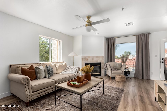 living room featuring wood finished floors, visible vents, ceiling fan, baseboards, and a tile fireplace