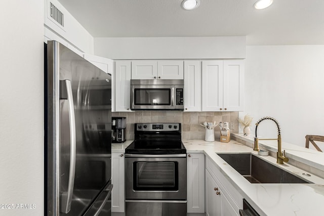kitchen with a sink, white cabinetry, visible vents, appliances with stainless steel finishes, and light stone counters