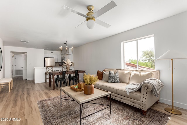 living room with ceiling fan with notable chandelier, baseboards, and light wood-style floors