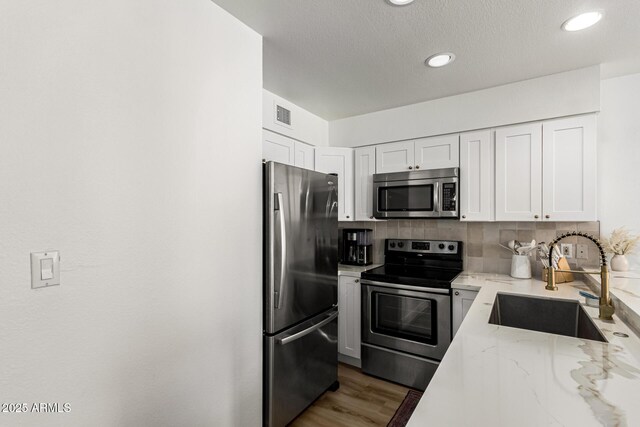 kitchen with a sink, decorative backsplash, white cabinets, light stone countertops, and appliances with stainless steel finishes