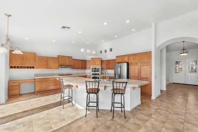 kitchen featuring stainless steel appliances, a high ceiling, a large island with sink, and hanging light fixtures