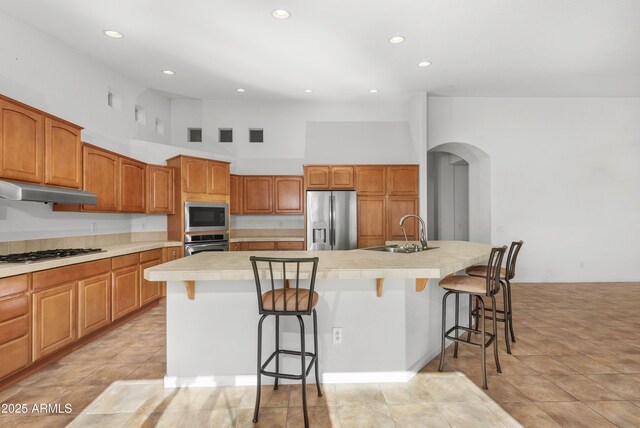 kitchen with a center island with sink, a high ceiling, stainless steel appliances, a breakfast bar, and sink