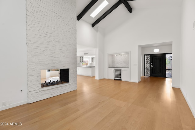 unfurnished living room with beverage cooler, beamed ceiling, a fireplace, light wood-type flooring, and high vaulted ceiling