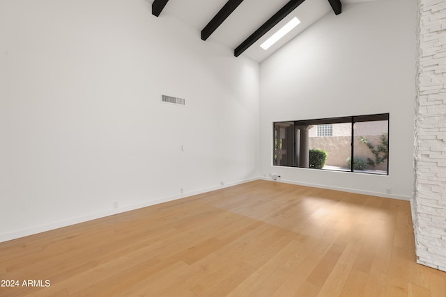 unfurnished room featuring beam ceiling, light hardwood / wood-style flooring, a skylight, and high vaulted ceiling