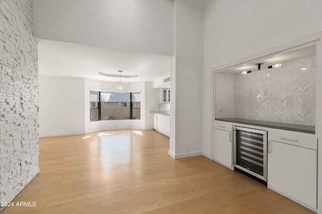 bar with backsplash, light wood-type flooring, beverage cooler, pendant lighting, and white cabinets