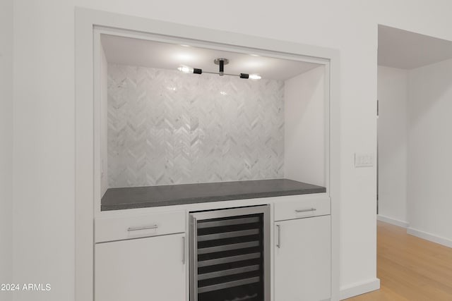 bar featuring wine cooler, white cabinets, light wood-type flooring, and backsplash