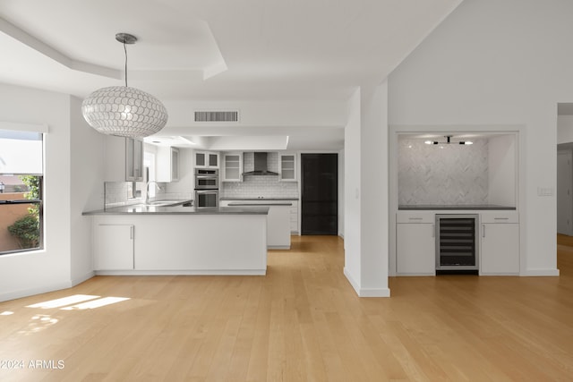 kitchen with decorative backsplash, hanging light fixtures, white cabinets, wall chimney exhaust hood, and beverage cooler