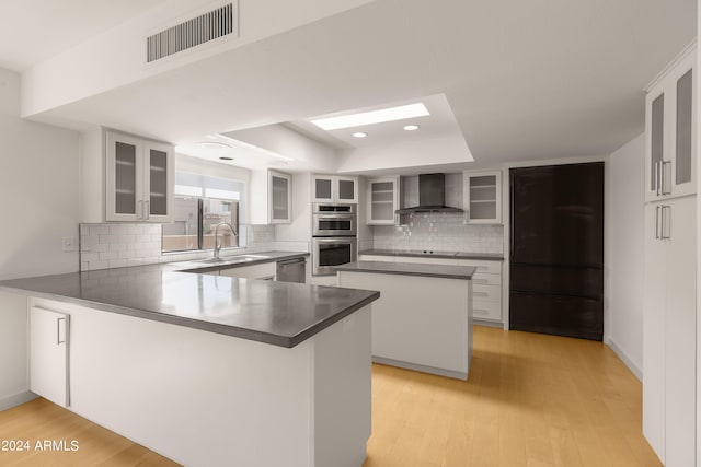 kitchen featuring white cabinets, wall chimney range hood, stainless steel appliances, sink, and kitchen peninsula