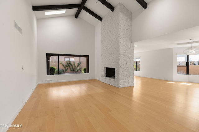 unfurnished living room featuring high vaulted ceiling, beam ceiling, light wood-type flooring, and a stone fireplace