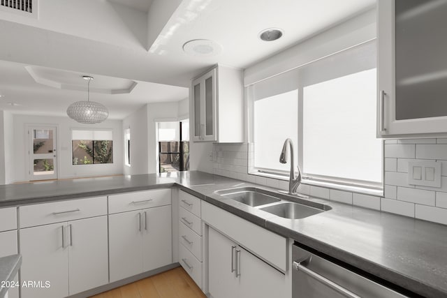 kitchen with white cabinetry, decorative backsplash, decorative light fixtures, stainless steel dishwasher, and sink