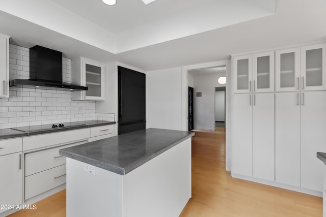 kitchen with white cabinets, wall chimney exhaust hood, a kitchen island, light hardwood / wood-style floors, and black electric cooktop