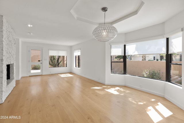 unfurnished living room featuring a tray ceiling, light wood-type flooring, a chandelier, and a fireplace