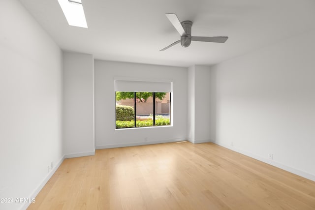 empty room featuring ceiling fan, a skylight, and light hardwood / wood-style flooring