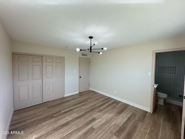 unfurnished bedroom with ensuite bath, hardwood / wood-style floors, an inviting chandelier, and a closet