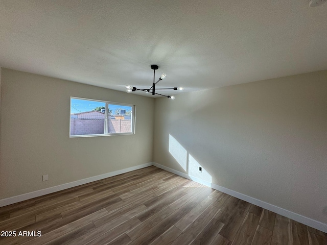 unfurnished room with an inviting chandelier, hardwood / wood-style floors, and a textured ceiling