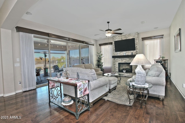 living room featuring a wealth of natural light, dark wood-type flooring, a stone fireplace, and ceiling fan